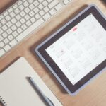 A tidy desk setup featuring a tablet displaying a calendar, keyboard, and stationary items.