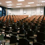 Empty university lecture hall with wooden chairs and large windows.
